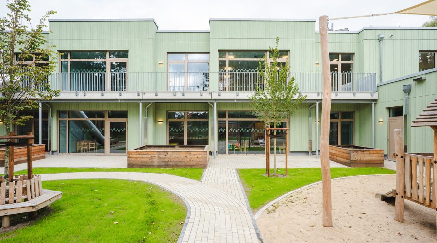 Moderne Kindertagesstätte in Holzbauweise mit grüner Fassade und Außenspielfläche – nachhaltiges Bildungsgebäude der Brüninghoff Group in Heiligenhaus.